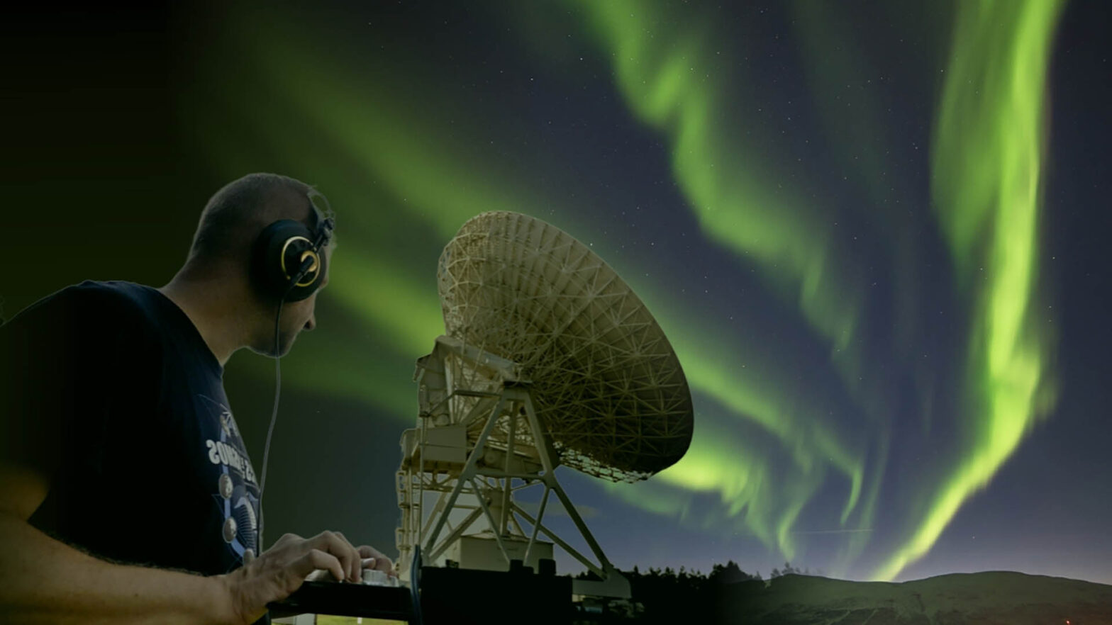 Fotomontaż. W tle zorza polarna w odcieniach zieleni na nocnym niebie. Na środku antena satelitarna teleskopu radiowego skierowana w prawo, za nią - tej samej wielkości mężczyzna od pasa w górę, ze słuchawkami na uszach i dłońmi na konsoli cyfrowej DJ, patrzący na tą antenę.