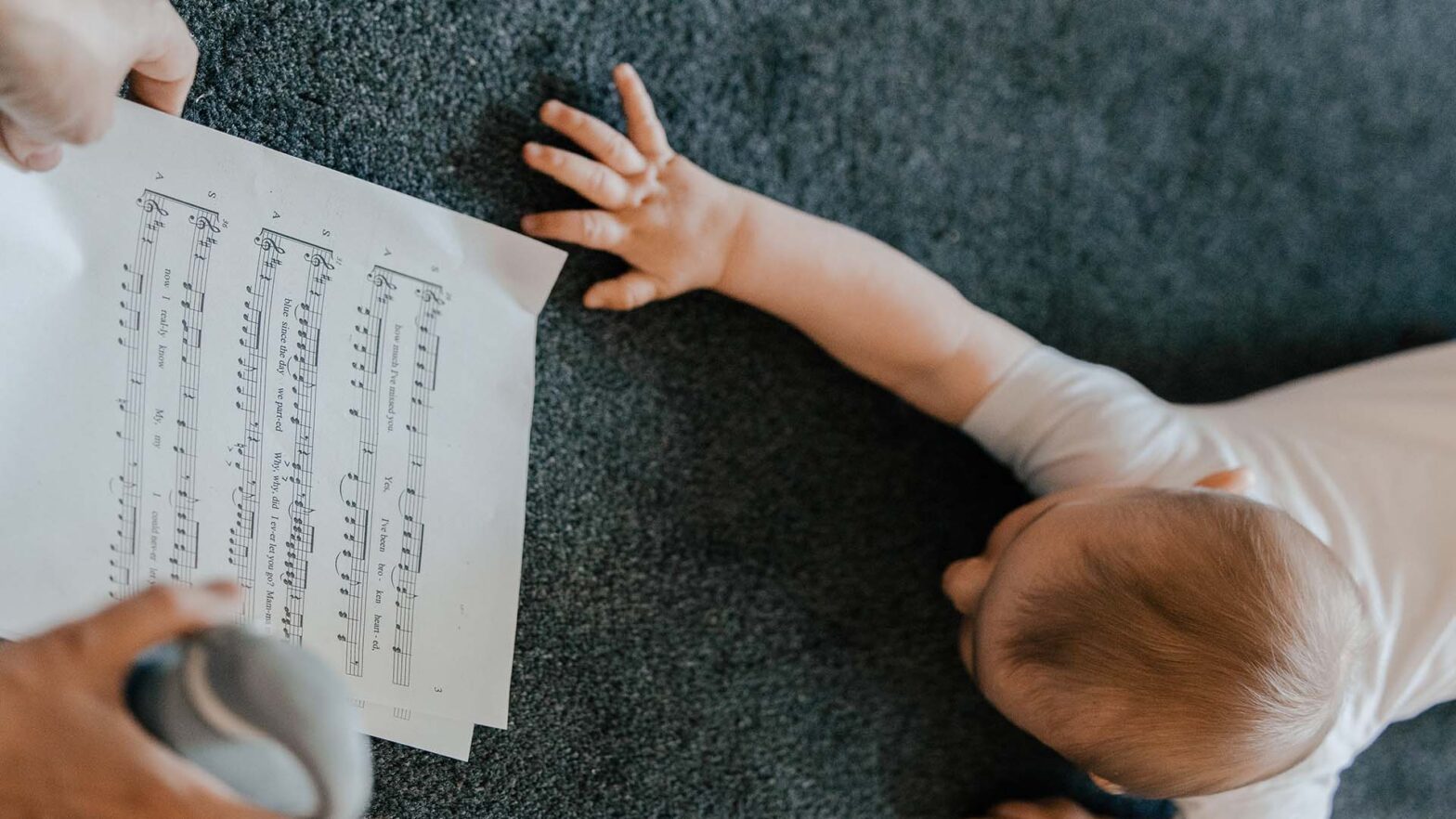 Małe dziecko raczkuje po dywanie i sięga ręką po kartkę z zapisem nutowym.