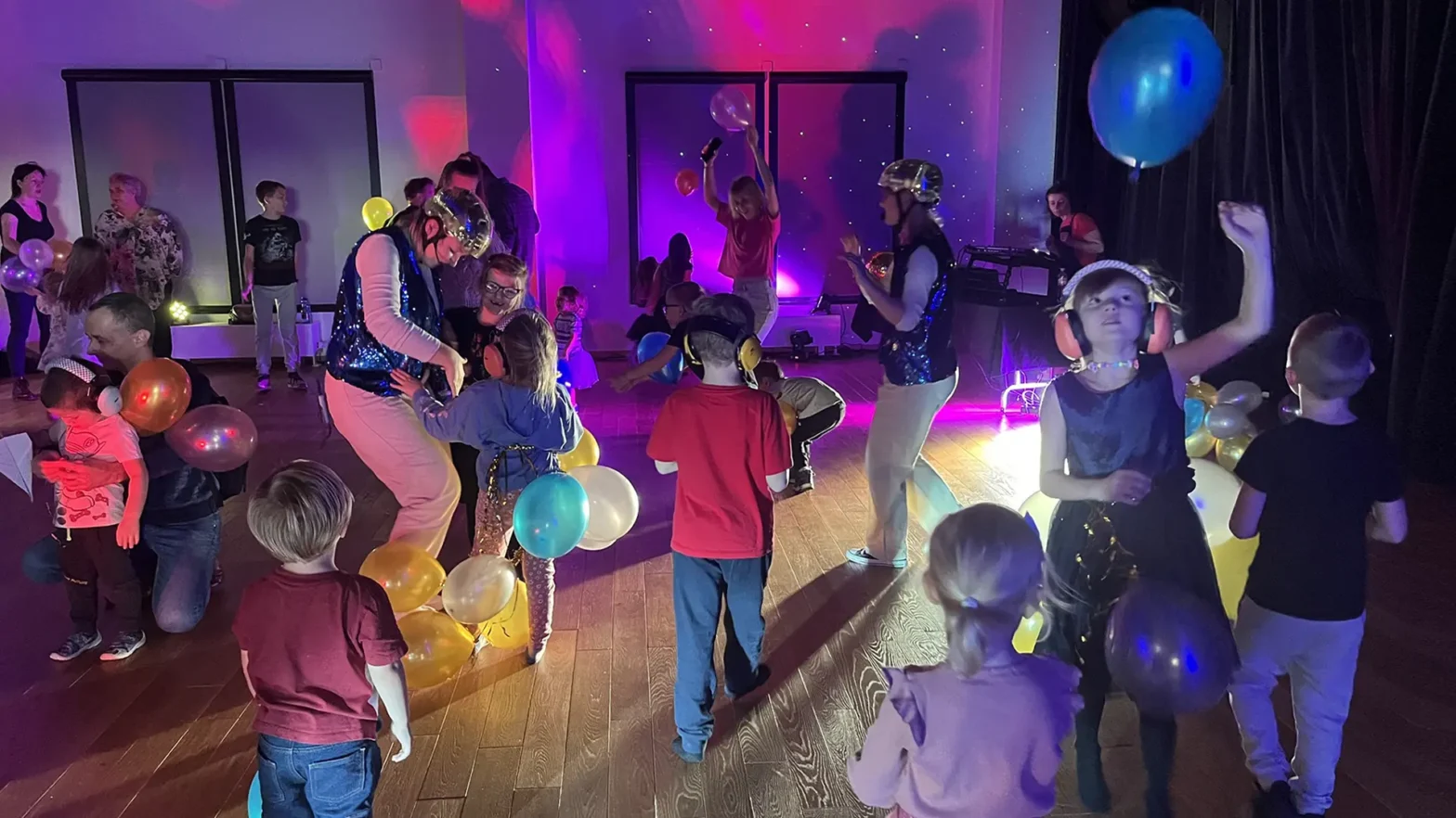 Grupa dzieci tańczy swobodnie w sali widowiskowej WOAKu, Podrzucają balony, bawią się i są radosne.