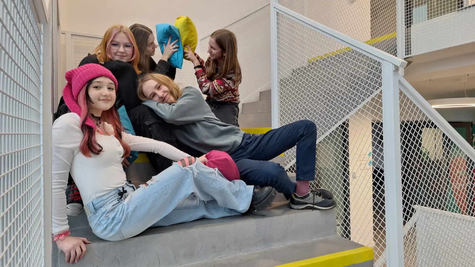 Zdjęcie przedstawia grupę młodych osób, siedzących na schodach i pozujących do zdjęcia