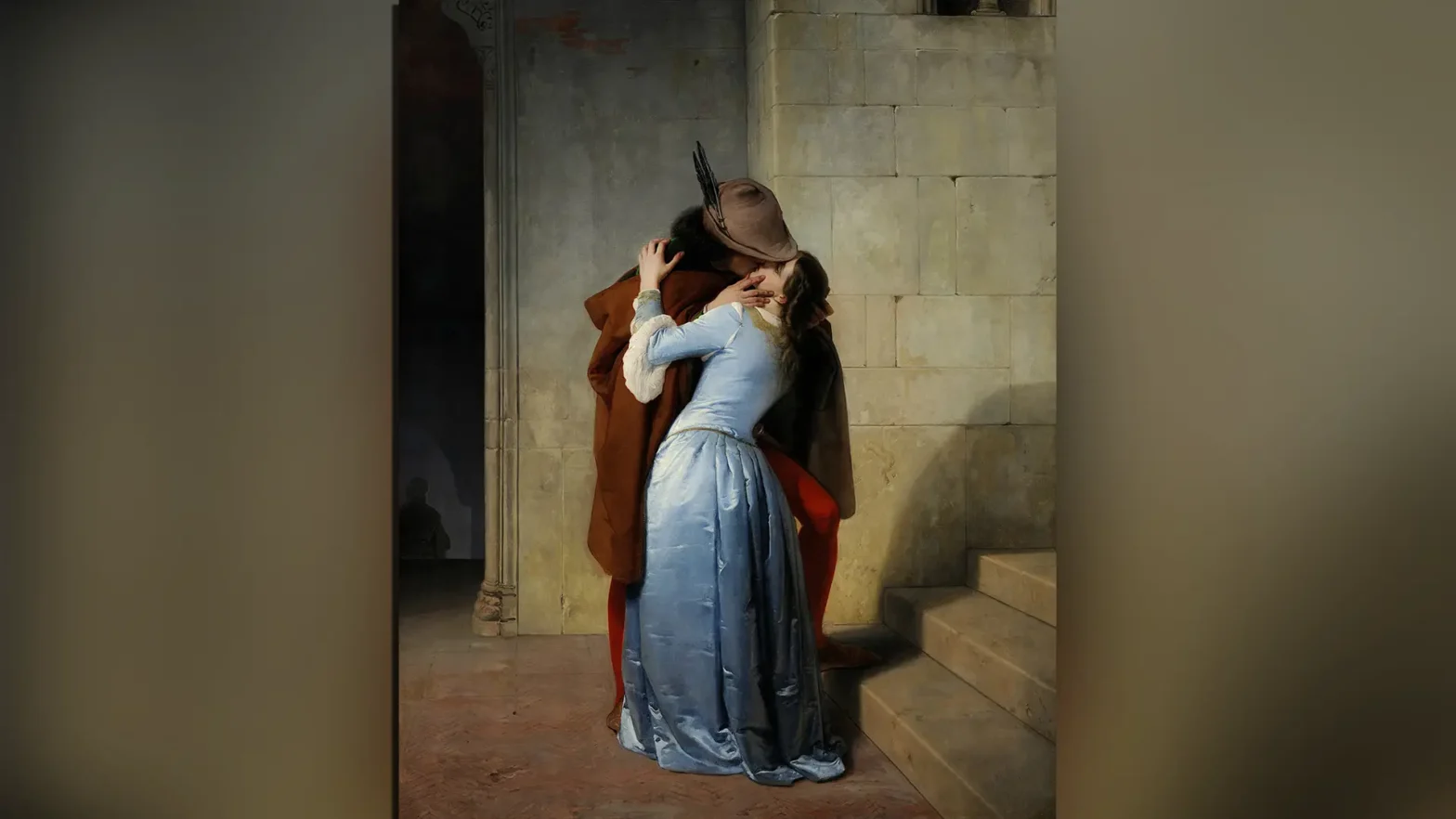 Obraz Pocałunek Francesko Hajeza. Obraz przedstawia parę, ubraną jak w średniowieczu, wymieniającą pocałunek. Mężczyzna w brązowej pelerynie i kobieta w niebieskiej sukni stoją u stóp schodów. Po lewej stronie znajduje się otwór, który prowadzi na parter, a w podświetlonym świetle jest cień sylwetki postaci, schodzącej po schodach. Para jest w centrum dzieła. Twarz mężczyzny jest ukryta pod kapeluszem, ale wyraźnie widać, że usta pary się stykają.