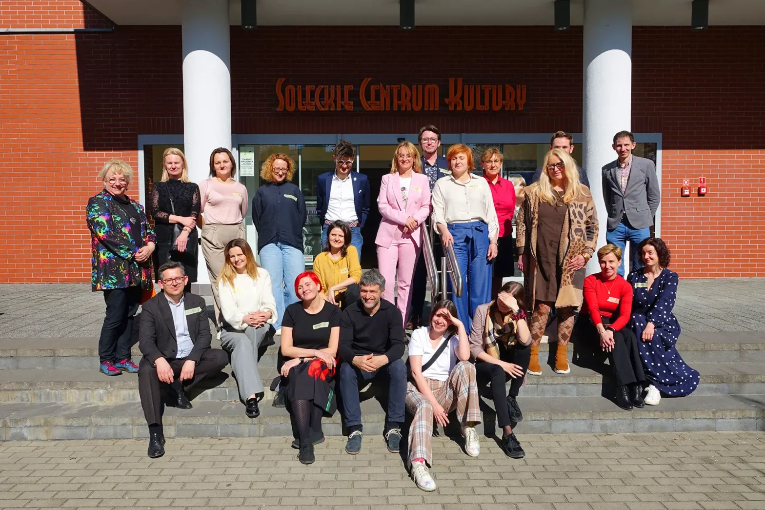 Grupa uczestników stojąca i siedząca na schodach przed wejściem do budynku Soleckiego Centrum Kultury, pozująca do wspólnego zdjęcia.